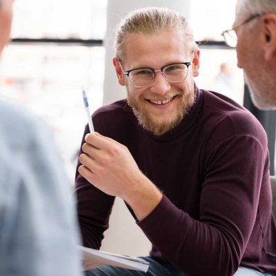 Männlicher Lehrer oder Dozent lächelt in einer Besprechung und tauscht sich mit Kolleginnen aus – Bildung und Jobs in Dresden